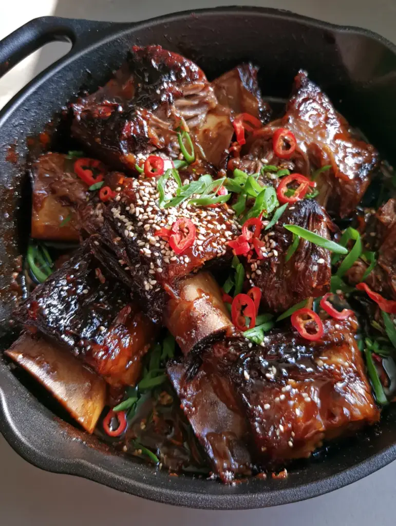 Top-down view of Sticky Asian Beef Short Ribs in a black skillet with rendered beef fat and caramelized sauce.