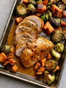 Close-up of glossy golden-brown honey dijon chicken slices with cracked black pepper and thyme on a sheet pan.