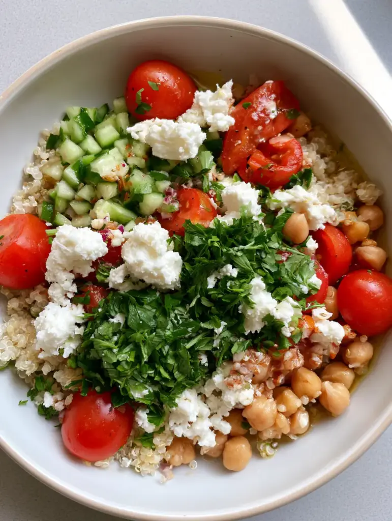 Mediterranean Quinoa Salad: The Ultimate Fresh & Healthy Meal Prep 1 Slightly angled view of a white ceramic bowl filled with Mediterranean Quinoa Salad, featuring feta cheese and parsley garnish.